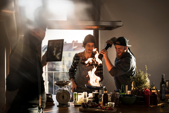 Friends flambeing food in a pan, producing a big flame, while friend is filming