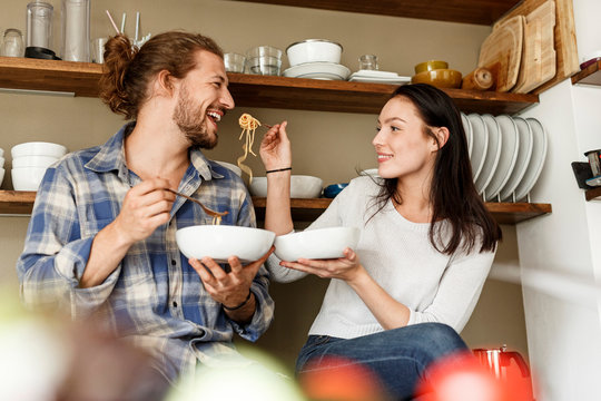 Happy couple sitting in kitchen, eating spaghetti