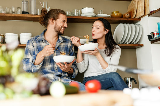 Happy couple sitting in kitchen, eating spaghetti