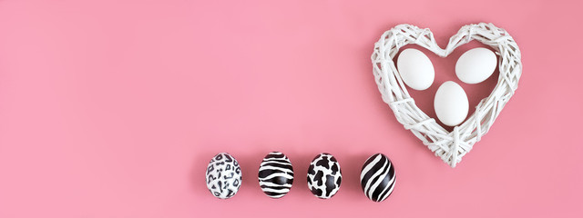 Easter eggs painted like zebra, cow, snow leopard. Three white eggs inside a white heart on pink background. Top view.