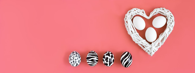 Easter eggs painted like zebra, cow, snow leopard. Three white eggs inside a white heart on coral background. Top view.