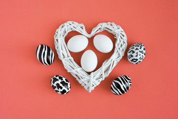 Easter eggs painted like zebra, cow, snow leopard. Three white eggs inside a white heart on coral background. Top view.