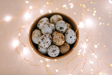 Quail eggs in a wooden plate on a pink background with golden lights. Easter concept.