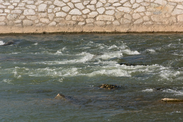 Fototapeta premium Big green river rapids and rock quay on a spring sunny day in city park. Natural background concept. Close up, selective focus