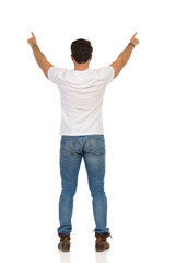 Young Man In Jeans And White T-shirt Is Standing And Showing Something. Rear View