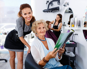 Young woman hairdresser in hair salon helping to senior woman choosing hairstyling