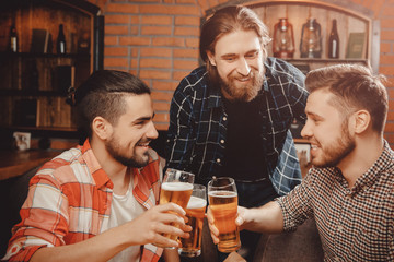 Three bearded men drinking beer Irish pub, clinking glasses toasting, chin-chin