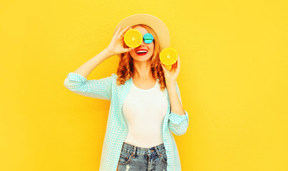 Summer portrait happy smiling woman holding in her hands slices of orange hiding her eyes in straw hat on colorful yellow background