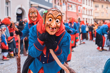 Funny witch in blue red robe leaning on the broom. Street Carnival in Southern Germany - Black Forest.