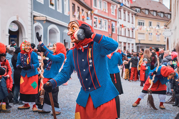 Funny witch in blue-red robe is using a shoe as a phone. Street Carnival in Southern Germany - Black Forest.