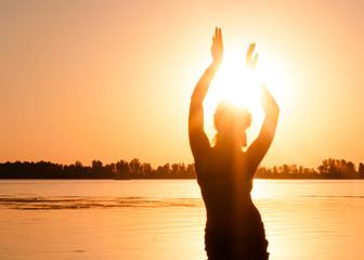 dark silhouette of woman dancing near river coast at dawn