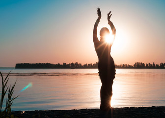 dark silhouette of dancing slim woman near big river coast at dawn