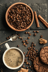 Black fried coffee beans in cafe with cookie and cake on dark textured background