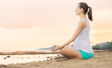 Fototapeta na wymiar young pregnant woman doing yoga on the beach