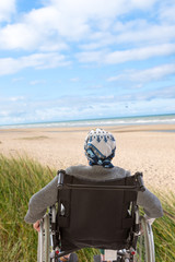 Disabled lifrstyle, invalid senior woman with headcarf on wheelchairs whith on foreground the sea,