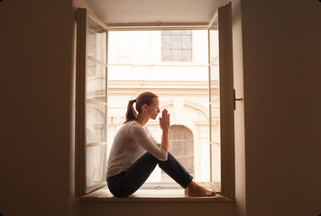 woman sitting on windowsill praying