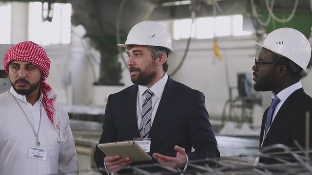 Panning shot of Caucasian engineers explaining their foreign visitors principles of building