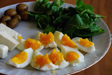 Coddled boiled eggs with season herbs cheese and olives on the white dish taken with natural light