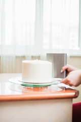 The confectioner smoothes the white cream on the biscuit cake using a culinary spatula. decorating the cake with cream, line the white cream on the cake.