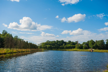 Beautiful still lake with trees on the horizon and white puffy clouds in the sky. Peaceful summer day at the cottage. Large green trees on a lake
