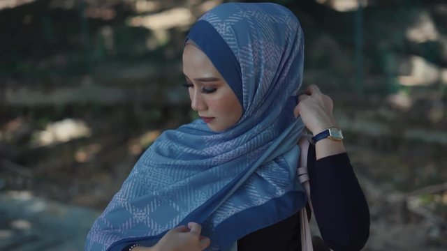 Portrait of attractive young Muslim woman in hijab walking around at green nature park.