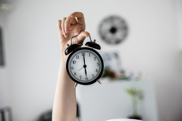 An outstretched female arm is holding an alarm clock. Daylight saving time concept.