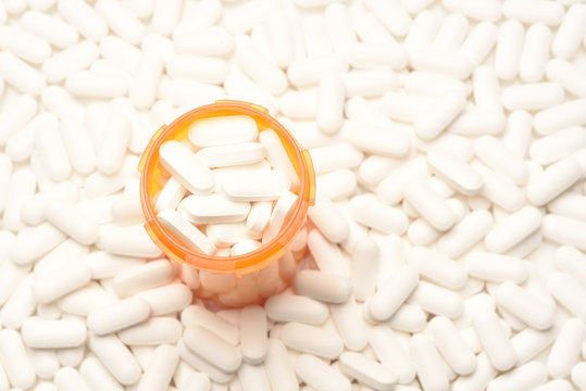 High angle view of a prescription bottled filled with pills surrounded by more of the same tablets