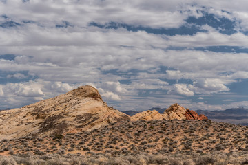 Desert landscape of red rocks under white fluffy clouds.
