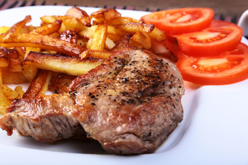 Grilled free-range beef steak with potato free, fresh tomatoes and sauce on a brown stone background