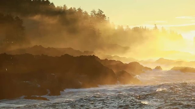 Waves crashing against the rocks on a coastline as the morning sun light casts a glow