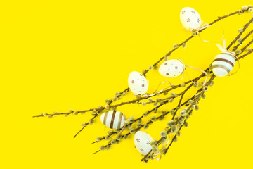 Fototapeta na wymiar Easter yellow background with eggs hanging on branches of catkins