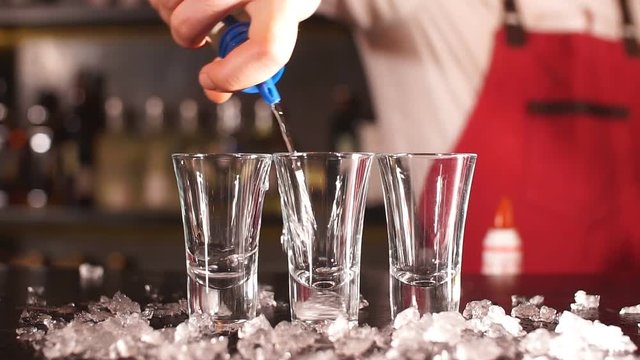 Professional male bartender serving the order, pouring alcoholic drink in a row of shot frozen glasses in a nightclub