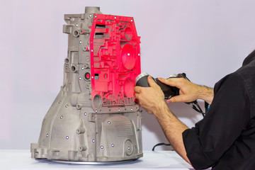 engineer or operator who emits pink light laser from a portable 3d scan (high accuracy equipment) to a transmission block of automotive part for inspection in factory