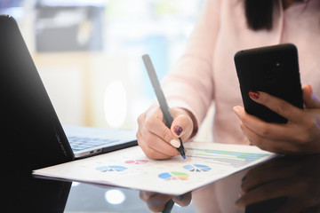 Business woman analysed report of profit finance data graph document with smart phone and laptop in her office