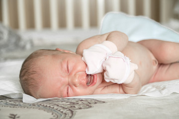 Newborn naked baby crying on the bed
