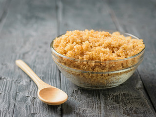 A bowl of boiled quinoa and a wooden spoon on a black wooden table.