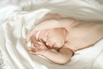 Fototapeta na wymiar Close up of a sleeping naked newborn baby girl on a white blanket