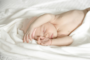 Close up of a sleeping naked newborn baby girl on a white blanket