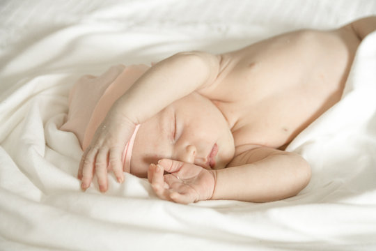 Close up of a sleeping naked newborn baby girl on a white blanket
