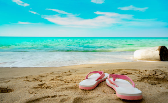Pink and white sandals on sand beach. Casual style flip-flop were removed at seaside. Summer vacation on tropical beach. Fun holiday travel on sandy beach. Summertime. Summer vibes. Relaxing time.
