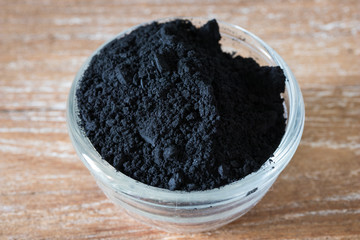 Close up of activated black charcoal powder in a glass bowl on wooden background