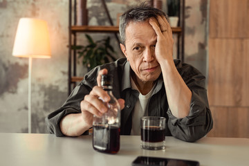 Desperate old alcoholic sitting in front of glass bottle with rom