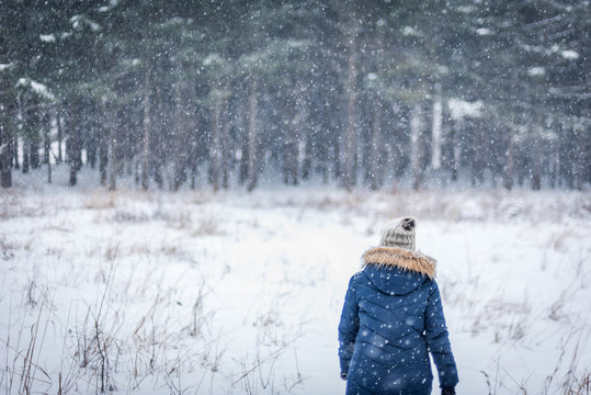 woman walking in winter woods with snow falling
