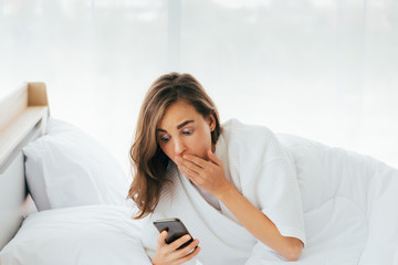 Amazed woman looking at smartphone on bed