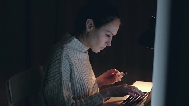 Female brunette  buying online shopping by credit card in home using notebook at  night. slowmotion.