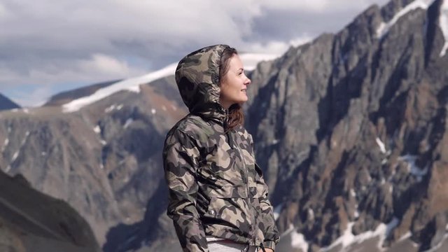 young woman on a background of mountains stands in a jacket with a happy smile. traveler