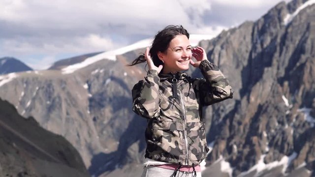 young woman on a background of mountains stands in a jacket with a happy smile. traveler