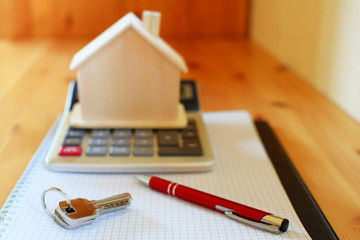 Paper notebook with calculator, house model keys and pen on wooden table.  House building, buying or renting new home planning concept.