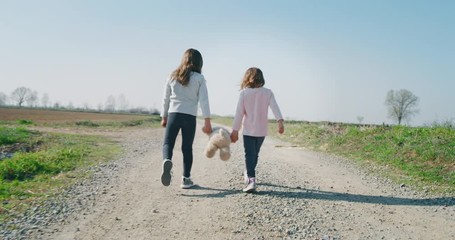 Authentic shot of two cute little girls sisters carefree walking on with teddy bear on a countryside background in a sunny day. - Powered by Adobe