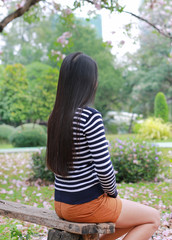 Naklejka premium Rear view Asian woman sitting on wood bench in the garden outdoor with looking out.